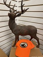 Side view of dark brown deer figurine with large antlers and orange hunting hat placed in front.