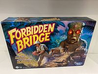 Front and side views of the Forbidden Bridge board game box, showing vibrant cover art with an explorer and a mechanical idol with glowing red eyes in a jungle setting.
