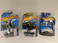 Three Hot Wheels cars in original packaging showing all vehicles from front and side angles: green vintage car with blower engine, green pickup truck, and silver futuristic car.