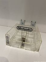 Front angle photo showing clear plastic shelf organizer with Nintendo logo and metal hooks at back
