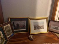 Six framed prints displayed leaning against a wall, different frame styles and sizes.