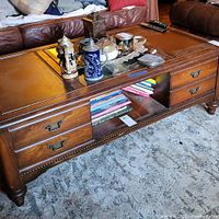 Front view of the wooden coffee table showing drawers, open shelf with books, and scratched surface.