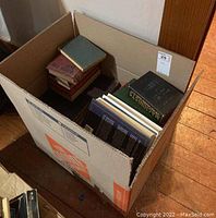 Wide angle shot of box filled with assorted sized books, some stacked in smaller piles inside the box