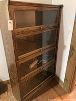 Full view of the four-tier wooden display cabinet with glass front doors, brass knobs, and a dark wood finish.
