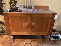 Front view of wooden cabinet showing carved handles and fluted vertical design on doors and sides. Cabinet has scratches and a patina consistent with heavy use.