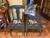 Two green wooden side chairs with black and gray plaid upholstery featuring white cat images on the seats, chairs showing scratches.