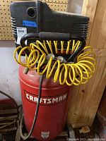 Full view of red Craftsman air compressor with yellow coiled hose around handlebar, mounted on wheels.