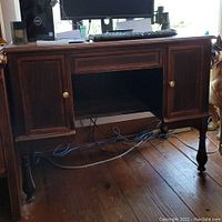 Full view of the solid wood desk with a computer monitor on top, showing cabinet doors with knobs, carved legs, and the desk overall condition.