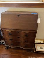 Front view of vintage wooden dresser with fold-down desk lid closed, showing metal latch and drawer handles.