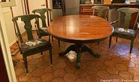Full view of Ethan Allen round dining table with four matching green arm chairs arranged around it on terracotta tile floor.