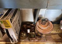 Photo of stacked clay planter saucers with several small brass pots and containers around them on a wooden surface.