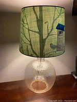Table lamp with clear textured glass base and green fabric shade with tree and bird design