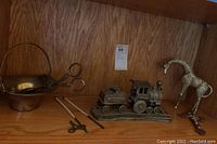 Photo showing a metal basket with handle and attached scissors, small cross, and heavy metal Santaville train figurine on wooden shelf.