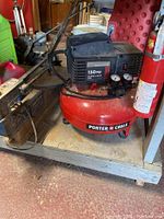 Porter Cable air compressor showing red tank, black motor housing, pressure gauges, and handle, placed on wood surface.