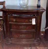 Front view of one dark wood Wynwood side table with three drawers showing decorative metal handles and keyhole details.