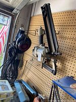 Wide angle view showing electric leaf blower, Porter Cable nailer, electric stapler, blue tool box and miscellaneous items in a garage with pegboard wall.