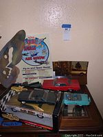 Toy cars arranged on wooden surface showing red muscle car, boxed die-cast car, and backdrop of air show poster.