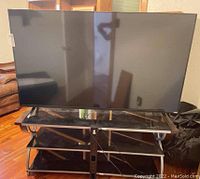 Front view of large Vizio 65-inch TV on black glass and wood TV table.