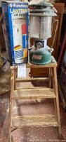 Photo of wooden ladder with vintage Coleman lantern and boxed 4-function lantern placed on top.
