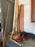 Wood boards and trim pieces with a metal carpenter's square resting diagonally. Some plywood sheets and narrower trim boards are visible.