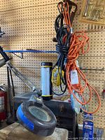 All four work lights and magnifying lamp hanging together on wood base with cords bundled and hanging, showing general overview of lot contents.