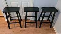 Three black wooden bar stools positioned side by side showing overall condition and style.