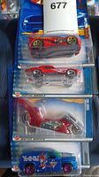 Four unopened Hot Wheels cars in original blister packages. Vehicles include a red sports car with flame and cartoon graphics, silver futuristic car, red-silver motorcycle, blue truck with graphics and purple wheels.