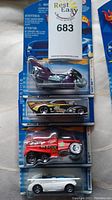 Lot of 4 brand new unopened Hot Wheels cars in packaging on blue backing cards with flame logos including a purple motorcycle, a black and yellow racing car, a red rescue truck, and a white convertible.