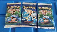 Three sealed booster packs (Venusaur, Blastoise, Venusaur) on a blue surface