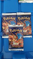 Three sealed booster packs on blue tray, front Charizard artwork visible