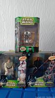 Front view showing all three Star Wars figures boxed: Boba Fett, Obi-Wan Kenobi with lightsaber, Darth Maul with double lightsabers, labels highlighting lights and attack features.