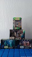 Four Star Wars figures in original boxes arranged on a blue surface against a white textured wall