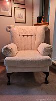 Front view of the cream upholstered chair with rolled arms, head cover, and carved wooden legs