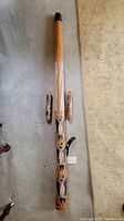 Full length view of wooden didgeridoo with upper natural wood finish and lower tribal painted design, with paired shakers on either side.