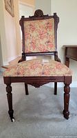 Front view of the Eastlake wooden chair showing the floral upholstery on seat and backrest and carved wood details.