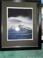 Close-up of framed photograph of ocean wave in black wood frame with beige mat, showing print and frame details