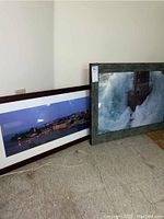 Two framed prints leaning against the wall on the floor showing the harbour scene and lighthouse pictures