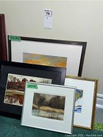 Four framed prints resting on floor leaning against a wall, showing various frames and art styles.
