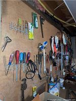 Wide view of pegboard with assorted hand tools and hardware items hung including screwdrivers, wrenches, saws, and other accessories.