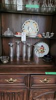 Photo of shelf with crystal butter dish, several pilsner glasses, silver-plated dish, small bowl, and other small dishes