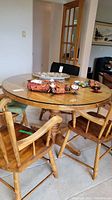 Round solid wood pedestal dining table with glass top and four attached wooden legs, showing wear and some scratches.