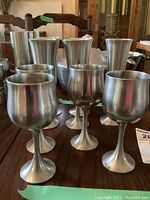 Photo showing 4 pewter wine goblets in front with 5 pewter champagne flutes behind on a wooden table.