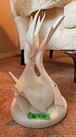 Full front view of the white porcelain bird sculpture showing two birds with elongated wings rising upward from a rounded base. The green tape indicates size 16x10 inches. The sculpture has a smooth glossy finish.