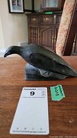 Front and side view of dark soapstone bird sculpture on a wooden surface with handwritten note showing measurements 8x2x3.