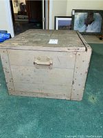 Photo of the vintage wooden shipping trunk placed on green carpet showing metal handle on side and riveted metal edge reinforcement