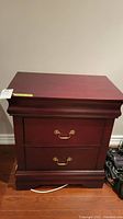 Front view of one dark cherry wooden bedside table with brass handles on two drawers, showing condition and size reference tag.