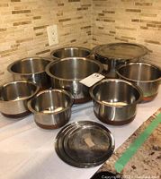 Eight stainless steel bowls with copper bases arranged on counter, some with flat lids on top or set aside.