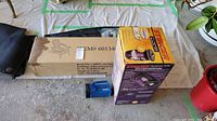 Photo showing boxed folding Adirondack chair kit, boxed bug zapper, and blue handheld vacuum on ground.