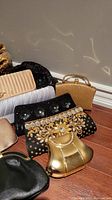 Closer view showing gold hard-case shaped bag, black embellished clutch with rhinestones and gold embroidery, beige quilted clutch and smaller satins.