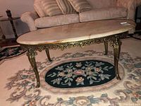 Side view image of the oval coffee table featuring its curved ornate metal legs and the stone top with beige and orange veining.